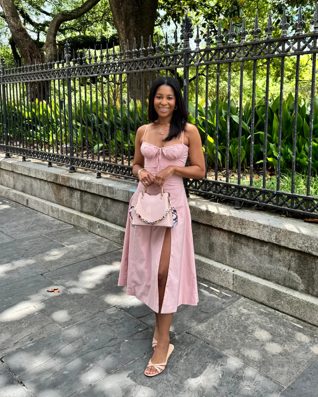 Indya smiling in a pink dress beside a wrought iron fence